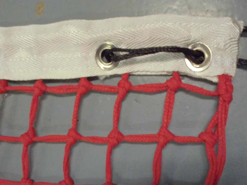 Bovenkant van het tennisnet rood. Goed te zien zijn de twee bevestigingsogen en de dubbele topmaas